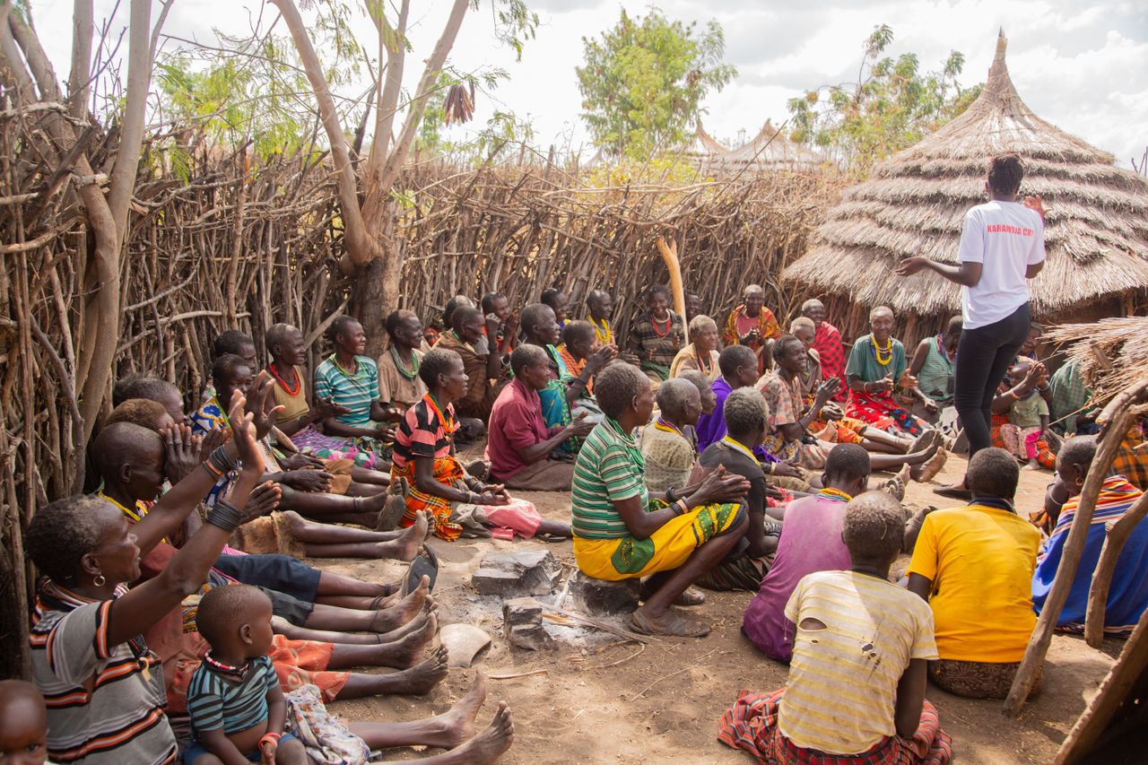 A gathering of people in traditional African village, sitting and interacting outdoors.
