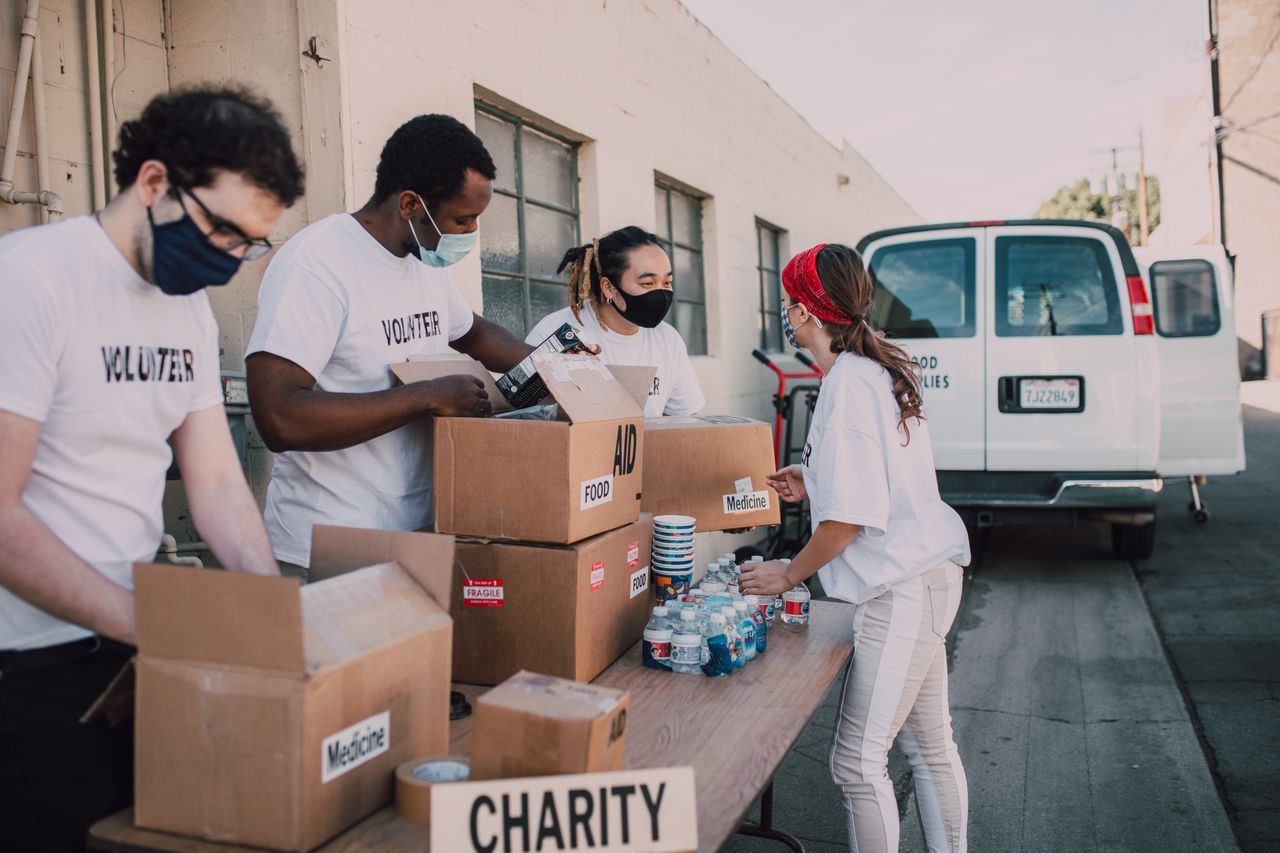 Group of volunteers wearing masks packing charity boxes outdoors during the pandemic.