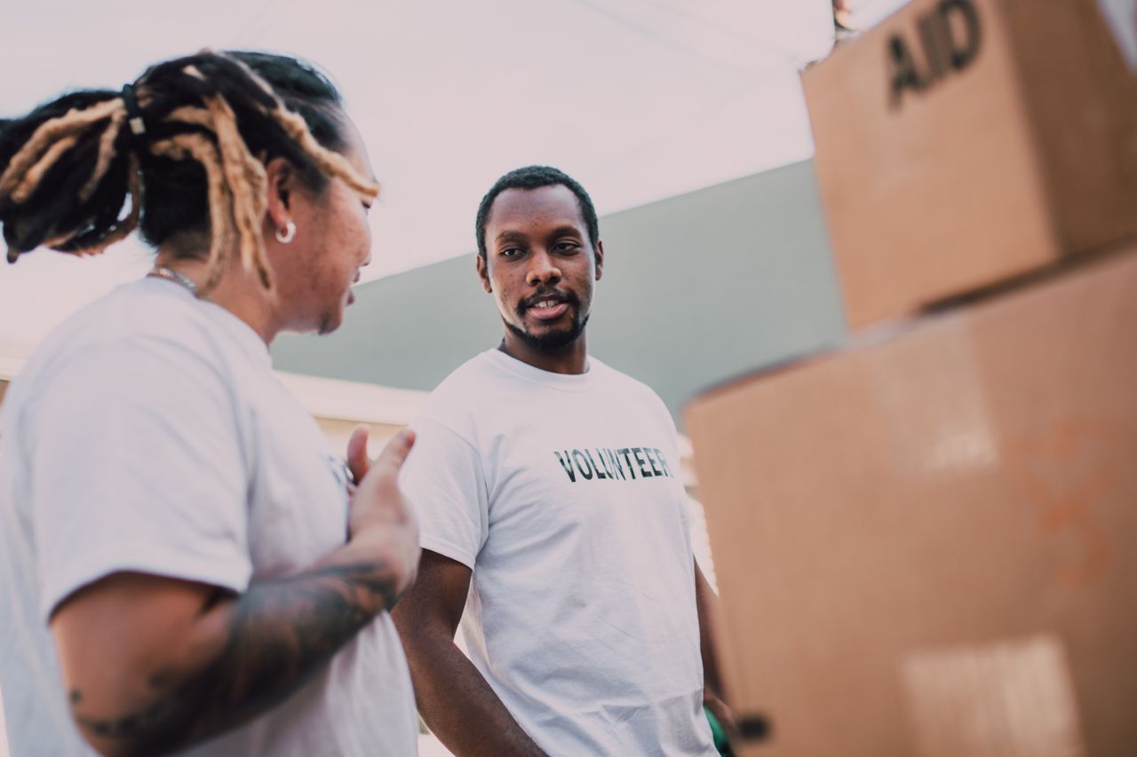Two volunteers organizing aid packages and communicating during an outdoor charity event.